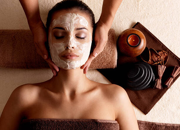 Spa massage for young woman with facial mask on face - indoors